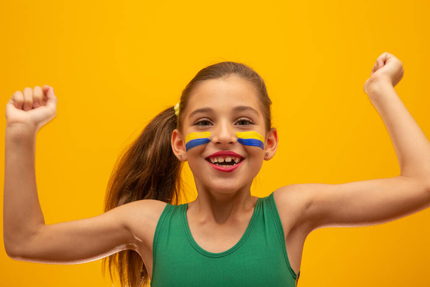Zwolennik piłki nożnej, drużyna Brazylii. Mistrzostwa świata. Piękna dziewczynka kibicuje swojej drużynie na żółtym tle - Zdjęcie, obraz