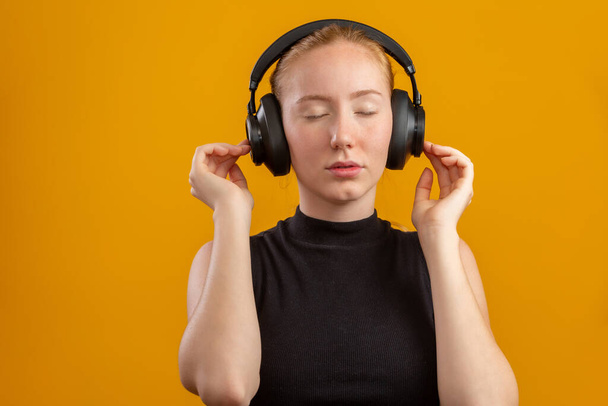 Happy and carefree excited redhead hipster girl like her new headphones, dancing with hands lifted up and smiling enjoy listening music over orange background, boost mood with favorite song. - Фото, изображение