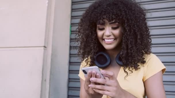 Stylish curly woman using smartphone posing on city background - Video