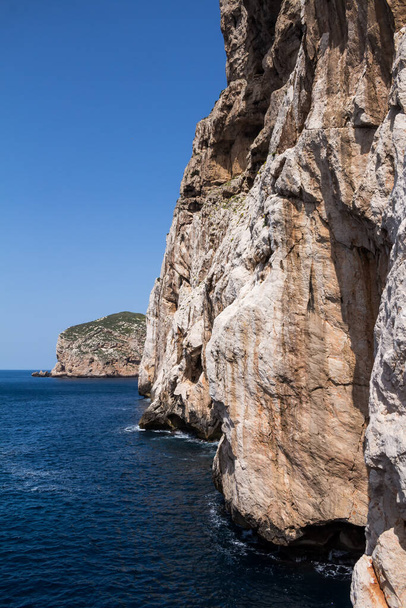 Ciemnoniebieska woda Morza Śródziemnego, skaliste klify Capo Caccia i wyspa Isola Foradada. Błękitne niebo. - Zdjęcie, obraz