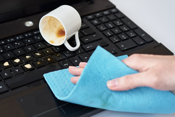 Рука очищает пролитый кофе на клавиатуре ноутбука тряпкой
 - Фото, изображение