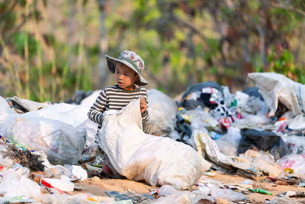 Ένα φτωχό αγόρι μαζεύει σκουπίδια από μια χωματερή στα περίχωρα. τα παιδιά εργάζονται σε αυτές τις τοποθεσίες για να κερδίσουν τα προς το ζην. Έννοια της φτώχειας. - Φωτογραφία, εικόνα