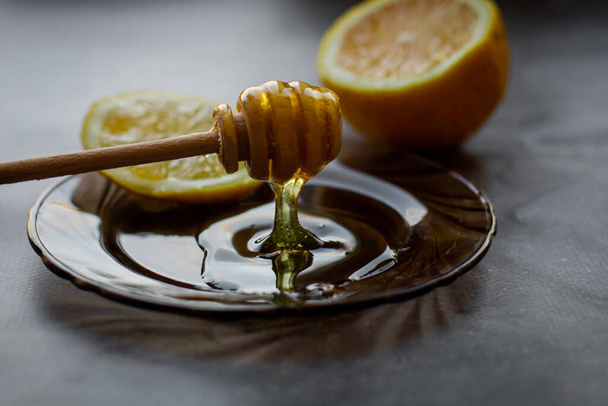 dripping honey on a saucer, gray background with lemon - Фото, изображение