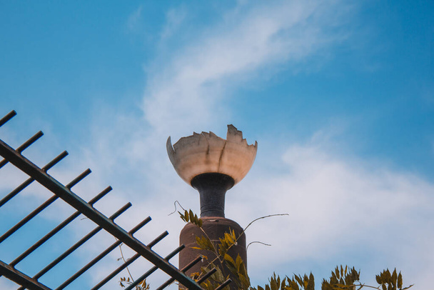 lámpara de calle rota junto a una valla de metal en un parque de la ciudad
 - Foto, imagen