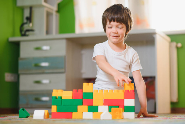 Children play with a toy designer on the floor of the children's room. Boy playing with colorful blocks. Kindergarten educational games. - Zdjęcie, obraz