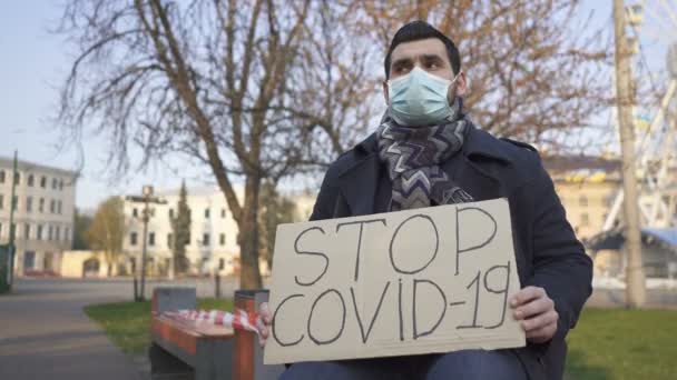 Pandemisch team. Man met medisch masker zitten op bank met poster op straat. - Video