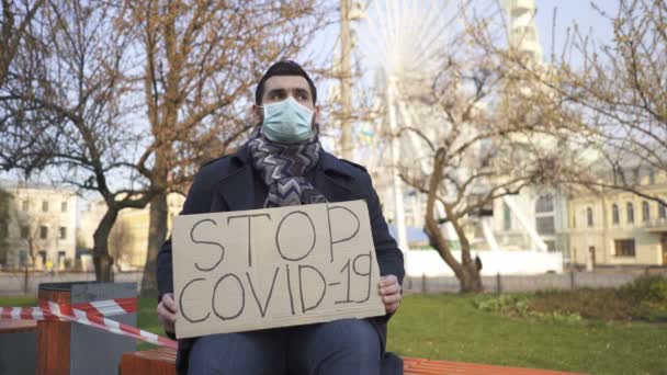 Equipa pandémica. Homem em máscara médica sentar no banco com cartaz na rua da cidade
. - Filmagem, Vídeo