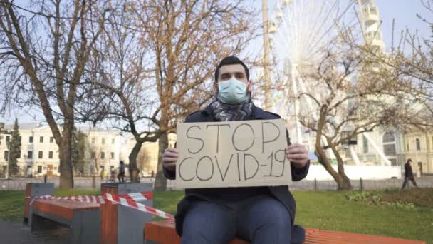  Ο άνθρωπος με την ιατρική μάσκα κάθεται στον πάγκο με αφίσα στην οδό Σίτυ. Ομάδα πανδημίας λέξεων - Πλάνα, βίντεο
