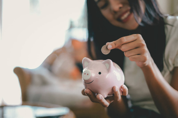 Glückliche junge Frau und Hand stecken Münze in Sparschwein, Finanz- oder Sparkonzept. - Foto, Bild
