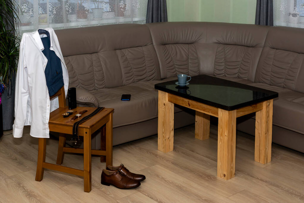 Мужская одежда и аксессуары на стуле в интерьере гостиной
 - Фото, изображение