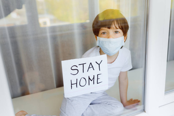 Stay at home quarantine coronavirus pandemic prevention. Sad child both in protective medical masks near windows and looks out window. View from street. Prevention epidemic. Coronavirus concept - Φωτογραφία, εικόνα