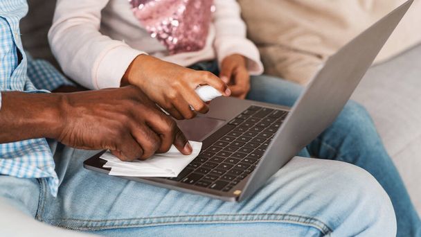 孫を持つアフリカ系アメリカ人の男性は、自宅でノートパソコンをきれいにするために消毒剤を使用して、閉じます。パノラマ - 写真・画像