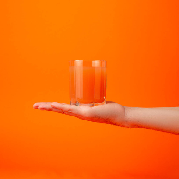 Ein Glas mit rotem Grapefruitsaft und Stroh in der Hand. Vereinzelt auf orangefarbenem Hintergrund. Konzept für gesunde Ernährung. Minimalismus - Foto, Bild