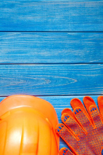 Orange hard hat and gloves on wooden vintage blue boards. Protective equipment for the builder - 写真・画像
