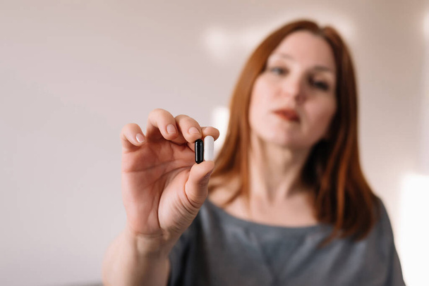 Erwachsene Frau hält schwarze und weiße Pillen in der Hand - Foto, Bild