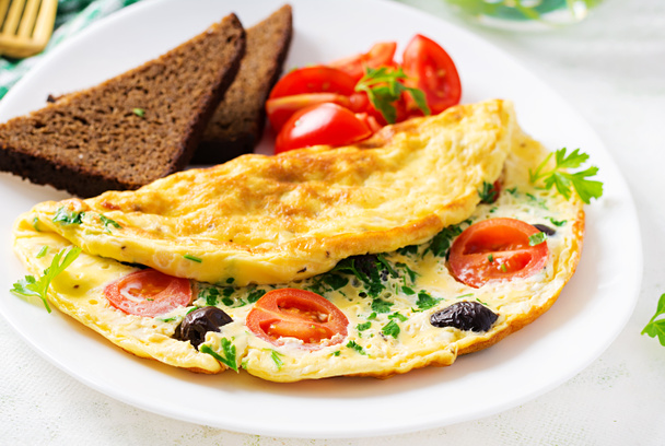Snídaně. Omeleta s rajčaty, černými olivami, tvarohem a zelenými bylinkami na bílém talíři. Frittata - italská omeleta. - Fotografie, Obrázek