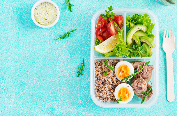 Zdravé jídlo. Oběd - Pohanková kaše, nakrájený tuňák, vařené vejce a čerstvý zeleninový salát v nádobě na modrém pozadí. Pohled shora, byt ležel - Fotografie, Obrázek