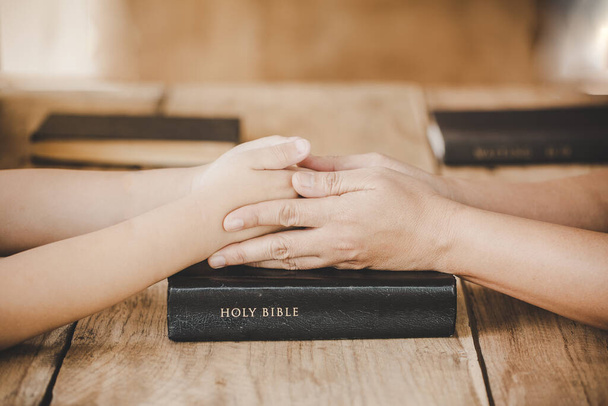 Couple mère et fils se tiennent la main et prient ensemble sur une table en bois avec la lumière du côté avec espace de copie pour votre texte
 - Photo, image