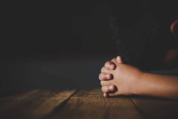 Молящиеся руки маленького мальчика на деревянном фоне стола
 - Фото, изображение