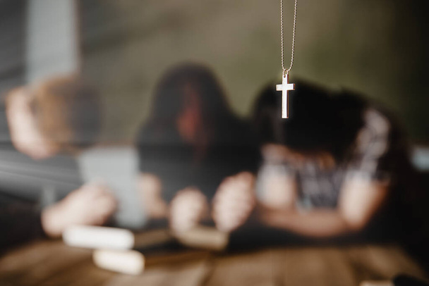 Srebrny krzyż w naszyjniku z modlącym się rodzinnym tłem. Mężczyzna, kobieta i dziecko.  - Zdjęcie, obraz
