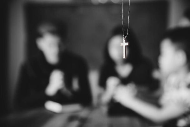 Stříbrný kříž v náhrdelníku s modlícím se rodinným pozadím. Muž, žena a dítě.  - Fotografie, Obrázek
