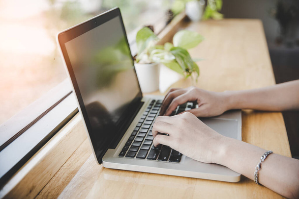 Vue latérale des mains de la jeune femme hipster occupée à travailler sur son ordinateur portable assis à une table en bois dans un café effet filtre rétro et style de couleur vintage
 - Photo, image