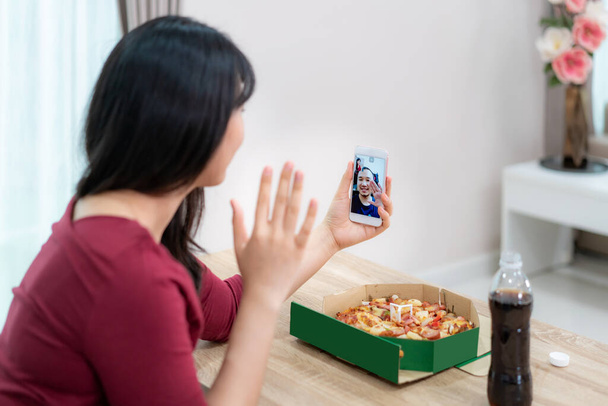 aziatische vrouw virtuele happy hour vergadering diner en het eten van pizza voedsel online samen met haar vriend in video conferentie met digitale tablet voor een online vergadering in video oproep voor sociale afstand - Foto, afbeelding