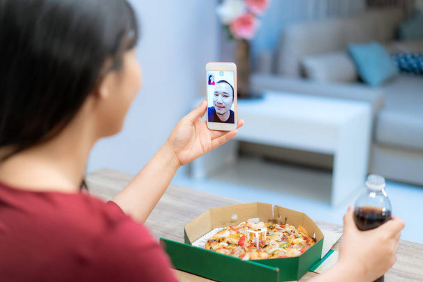 Asian woman virtual happy hour meeting dinner and eating pizza food online together with her boyfriend in video conference with digital tablet for a online meeting in video call for social distancin - Photo, Image