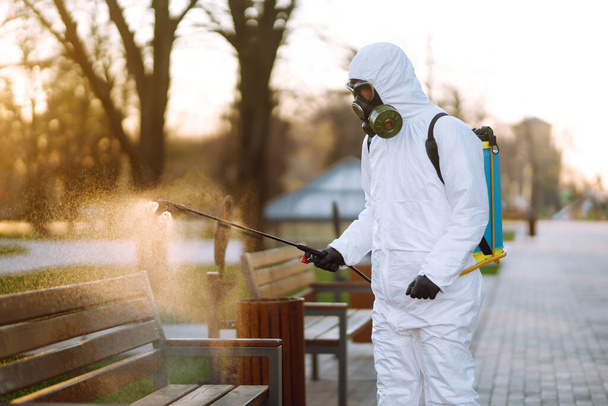 Man in protective suit disinfecting  bench in the public park in quarantine city. Infection prevention and control of epidemic.  Covid -19. - Foto, imagen