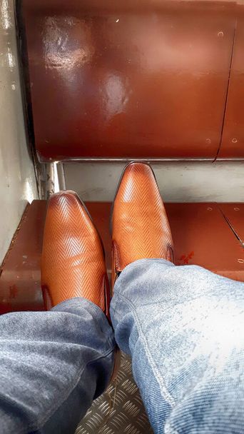 Dies ist ein Bild von einem Mann, der während einer Zugfahrt ein Paar braune Schuhe trägt. - Foto, Bild