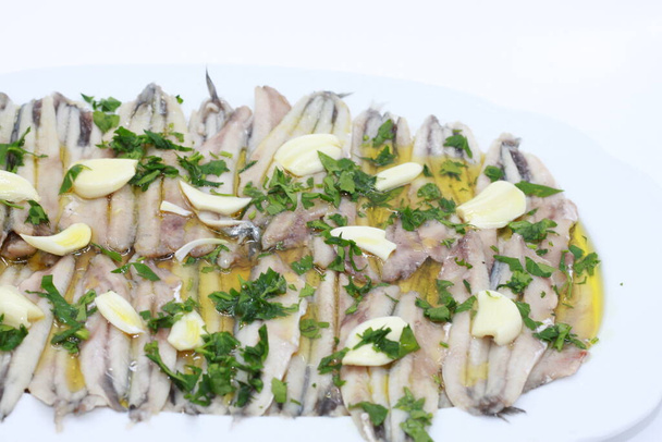Анчоусы с оливковым маслом, чесноком и уксусом на белом подносе
 - Фото, изображение