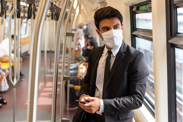 Geschäftsmann mit weißer Gesichtsmaske während der Zugfahrt, neuer normaler Lebensstil während der Covid-19-Pandemie - Foto, Bild