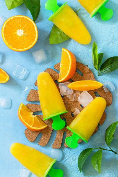 オレンジジュース、フルーツアイス、ブルーストーンやスレートの背景にロリポップと自家製のアイスポプシクル。トップ表示フラットレイアウトの背景. - 写真・画像