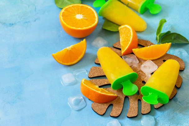 Homemade popsicles with orange juice, fruit ice, lollipops on a blue stone or slate background. Copy space. - Foto, Imagen