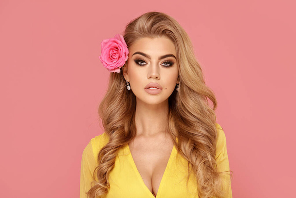 Closeup beauty portrait of attractive young beautiful blonde woman with roses. A girl with light wavy hair. Posing on a pastel pink studio background. - Fotoğraf, Görsel