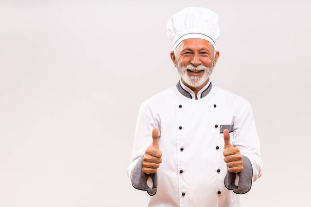 Portrait of  senior chef showing thumb up on gray background. - Foto, afbeelding