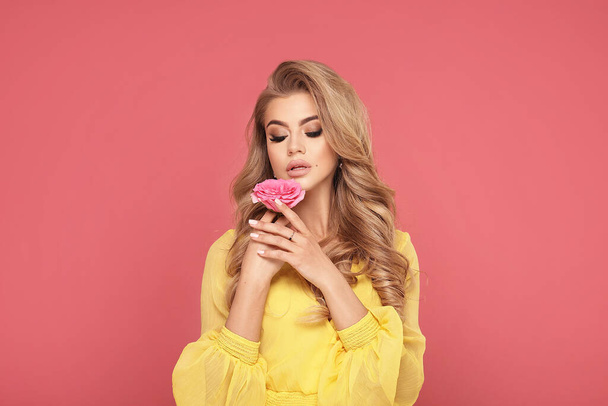 Closeup beauty portrait of attractive young beautiful blonde woman with rose. A girl with light wavy hair. Posing on a pastel pink studio background. - Φωτογραφία, εικόνα