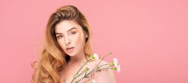 Beauty portrait of natural young redhead woman with meadow flowers. Girl with freckles on face posing on pastel pink background. - Photo, image