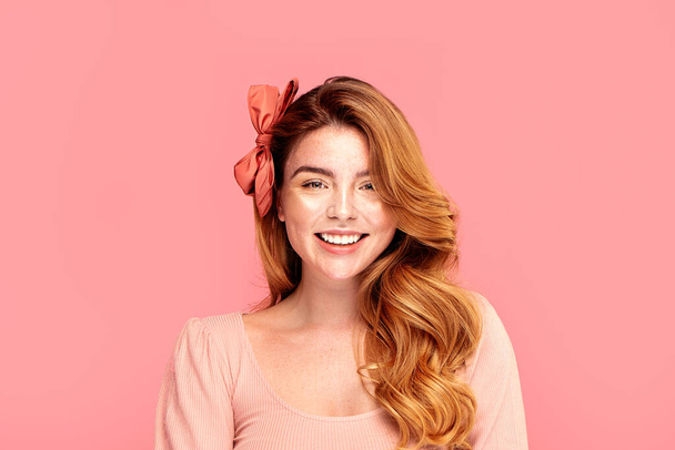 Beautiful face of young caucasian redhead woman. Gorgeous girl with a creative hairstyle isolated on pink pastel background. Natural face with freckles.Smiling lady - Foto, imagen