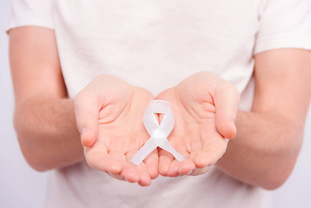 Koncepcja choroby onkologicznej. Mężczyzna w białej koszulce z białą wstążką jako symbolem raka płuc w rękach. - Zdjęcie, obraz