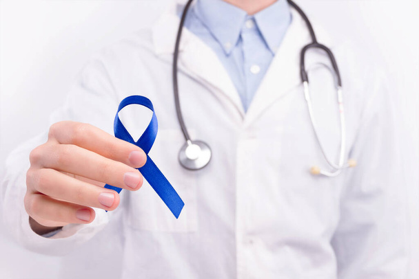 Onkológiai betegség koncepció. Az orvos fehér köpenyt és sztetoszkópot visel, sötét kék szalagot tartva a bélrák szimbólumaként..  - Fotó, kép