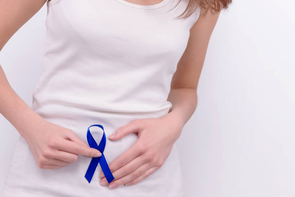 Oncologische ziekte concept. Meisje draagt witte top met blauw lint als symbool van darmkanker voor haar maag - Foto, afbeelding