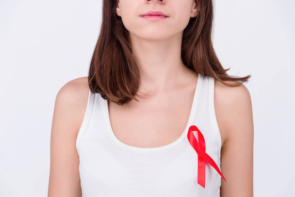 Safe sex / healthcare concept. Girl woman female wearing white top with pinned red ribbon as a symbol of hiv aids isolated on white background - Photo, Image