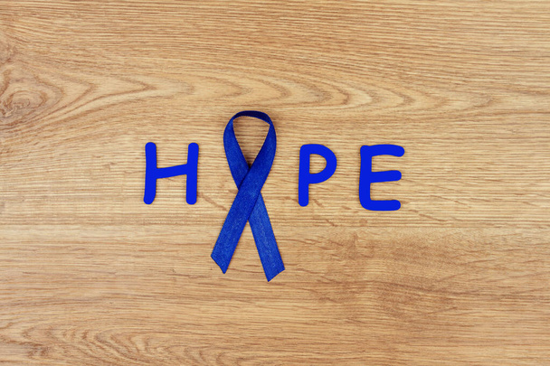 腫瘍疾患の概念。木製の背景に腸癌の象徴として青いリボンで書かれた言葉「希望」 - 写真・画像