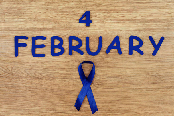 Всемирный день борьбы с раком. Голубая лента как символ рака кишечника изолирована на деревянном фоне
. - Фото, изображение