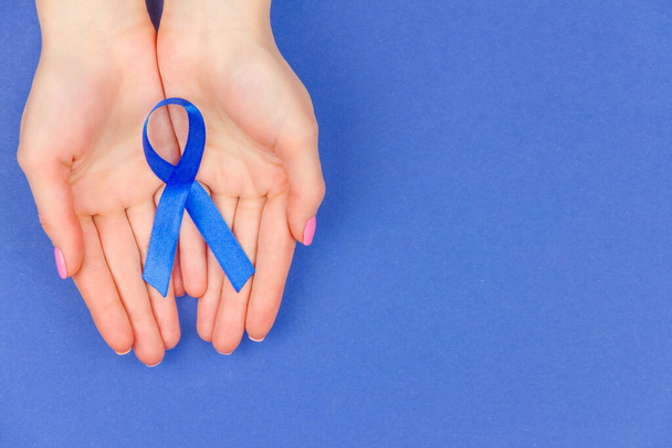 Ογκολογική έννοια της νόσου. Χέρια κρατώντας μπλε κορδέλα ως σύμβολο του καρκίνου του εντέρου σε μπλε φόντο - Φωτογραφία, εικόνα