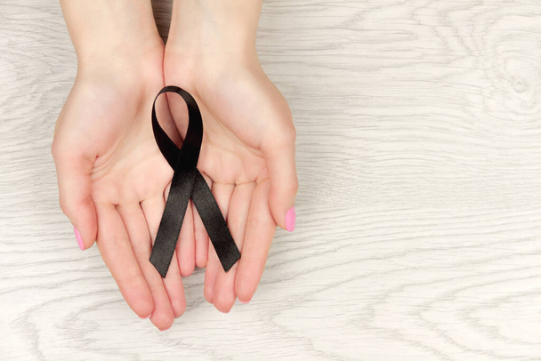 Oncologische ziekte concept. Handen met zwart lint als symbool van melanoom.  - Foto, afbeelding