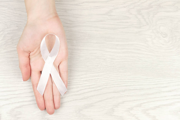 Ογκολογική έννοια της νόσου. Χέρι κρατώντας λευκή κορδέλα ως σύμβολο του καρκίνου του πνεύμονα - Φωτογραφία, εικόνα