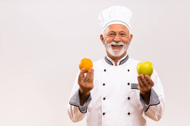 Portrait of senior chef shows fruit on gray background. - Foto, imagen