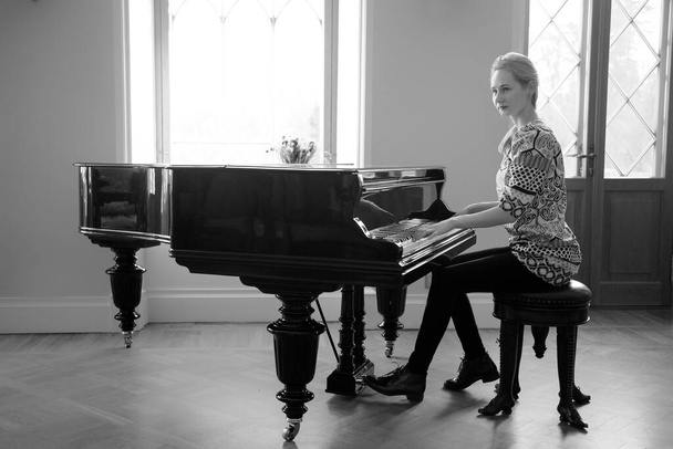 黒と白のイメージ – 城の窓の前でフォルテピアノを演奏するピアニストの女性。女性の平等と成果の概念. - 写真・画像
